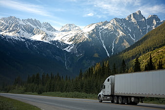 White semi-truck driving on highway with snow-capped mountains