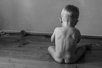 Black and white photo of a toddler sitting alone on wooden floor