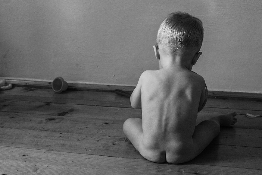 Black and white photo of a toddler sitting alone on wooden floor