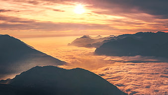 Sunset over mountain peaks above sea of clouds