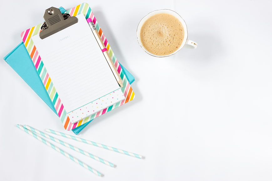 Flat lay of colorful clipboard, coffee cup, and striped straws on white background