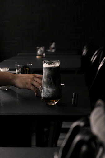 Hand holding glass of charcoal latte in dark cafe