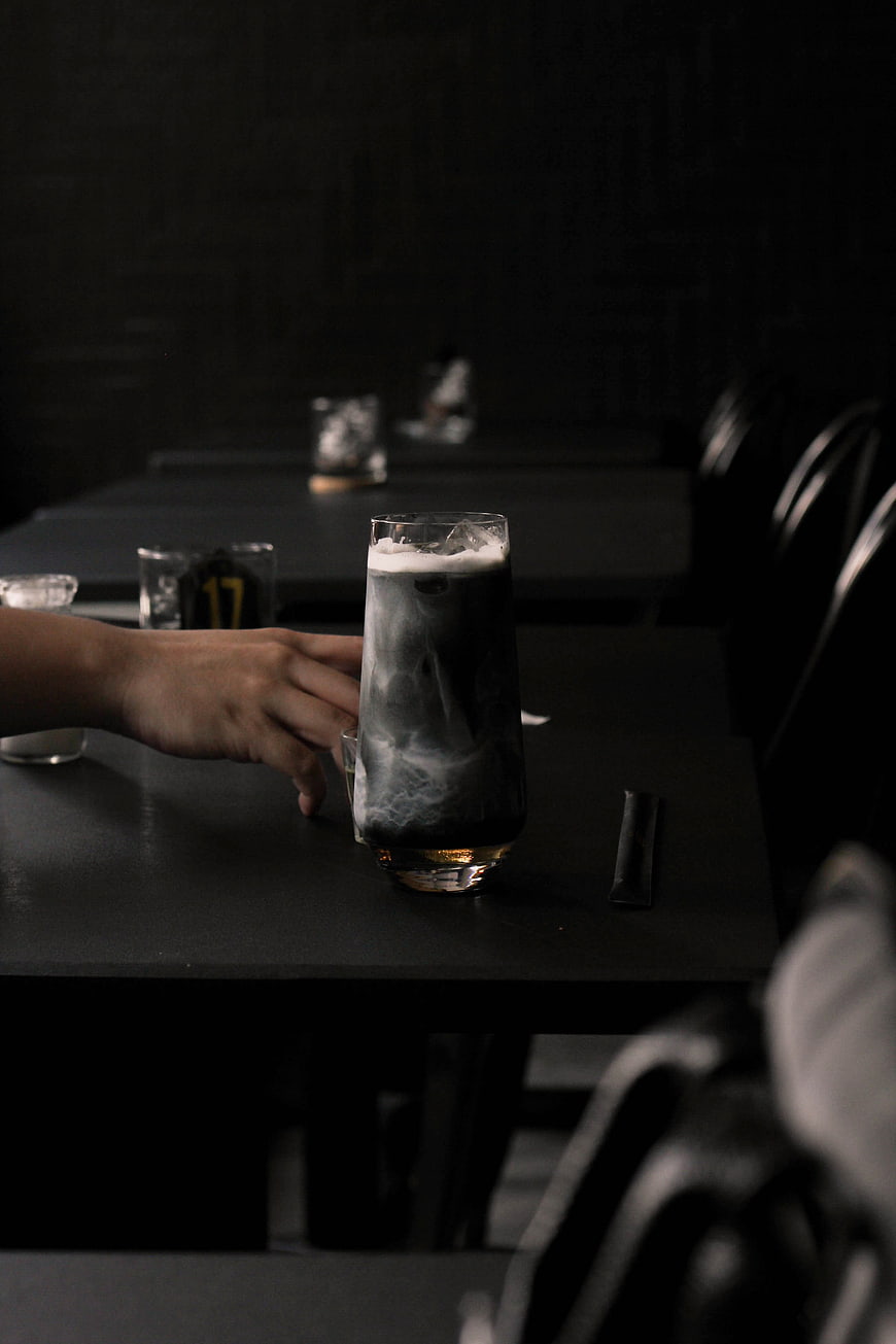 Hand holding glass of charcoal latte in dark cafe