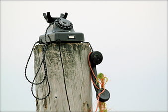 Vintage black rotary telephone mounted on a weathered wooden post