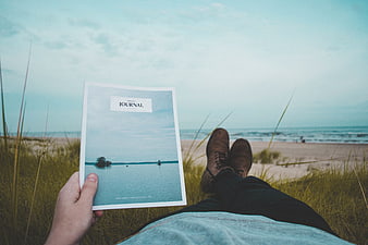 Person reading journal on beach dunes with ocean view