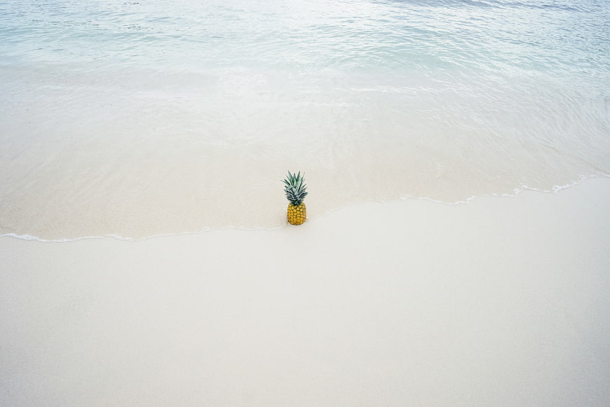 Lone pineapple on white sand beach with ocean waves
