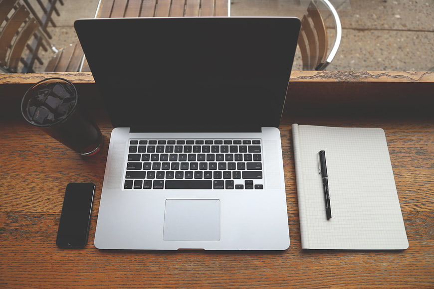 Top view of laptop, notebook, and iced coffee on wooden table