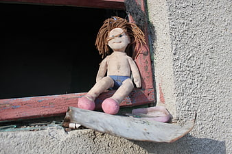 Abandoned handmade doll sitting on a weathered red window sill