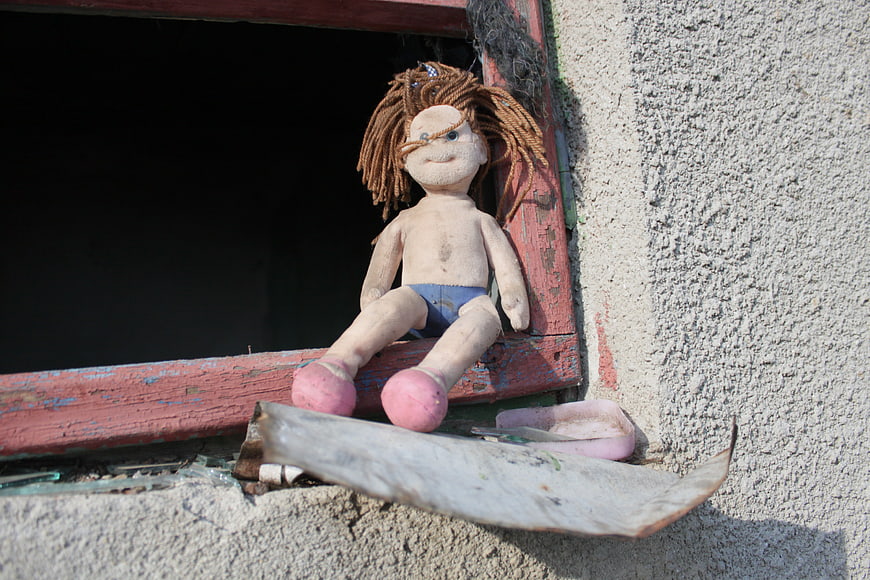 Abandoned handmade doll sitting on a weathered red window sill