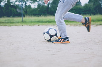 Close-up of soccer player kicking ball on sand