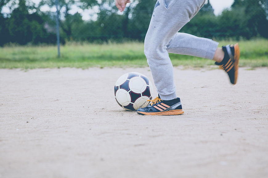 Close-up of soccer player kicking ball on sand