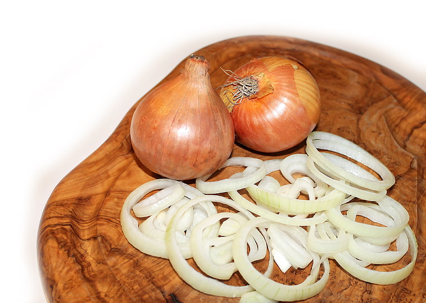 Fresh whole and sliced onions on a wooden cutting board