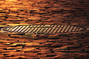 Golden Manhole Cover On Wet Cobblestone Street At Sunset