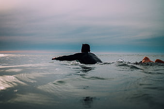Surfers paddling in ocean at sunset