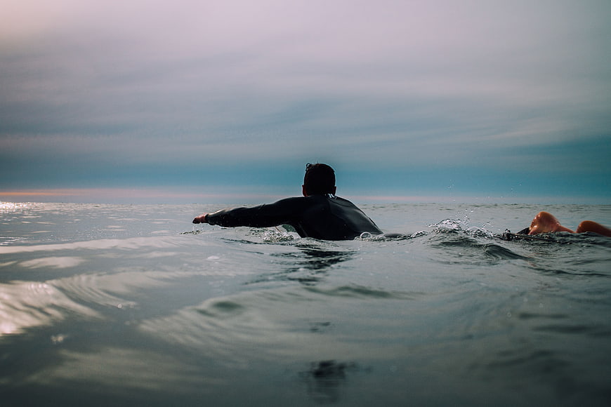 Surfers paddling in ocean at sunset