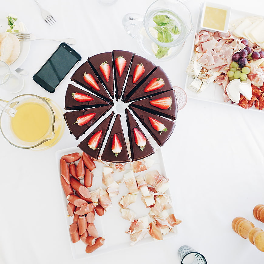 Top view of chocolate cake and charcuterie spread on white table