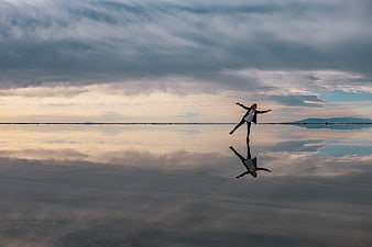 Woman jumping on reflective salt flat at sunset
