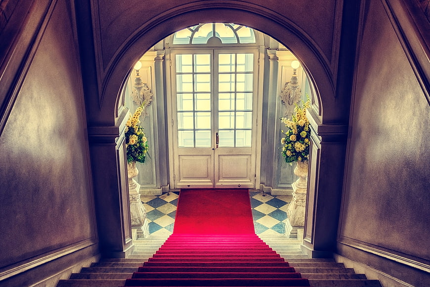 Grand Interior Staircase With Red Carpet Leading To Elegant Entrance