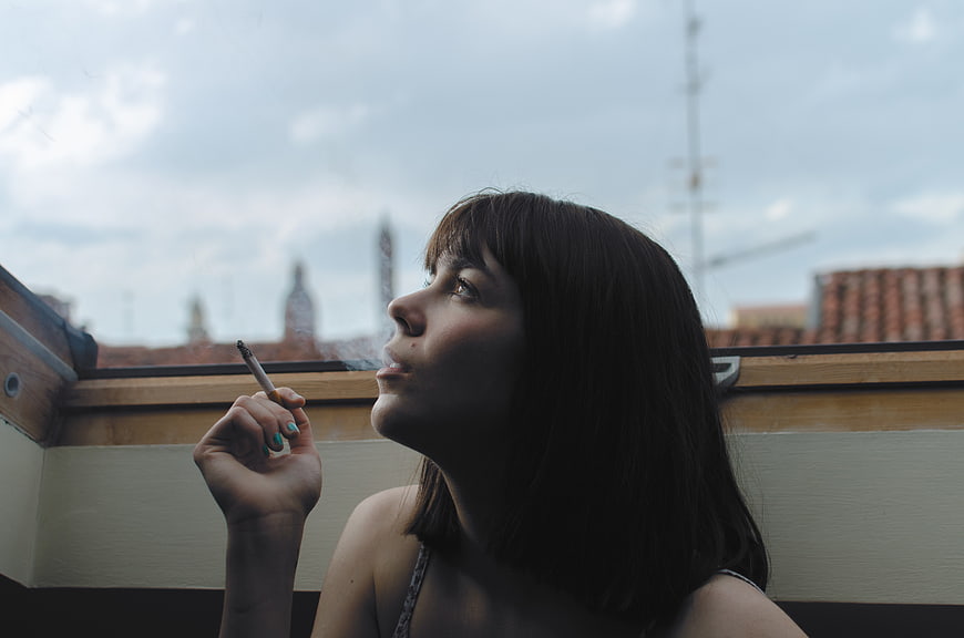 Woman smoking cigarette on rooftop with city skyline