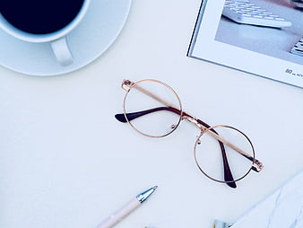 Flat lay of rose gold glasses, coffee, and pen on white desk