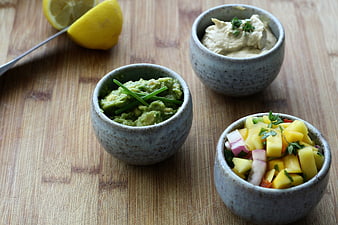 Guacamole, Hummus, and Mango Salsa in Ceramic Bowls on Wooden Table