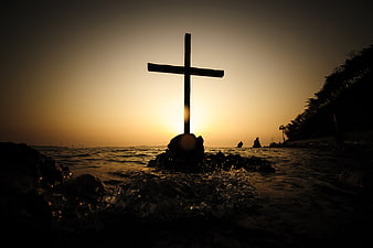 Silhouette of Cross on Rocky Shore at Sunset