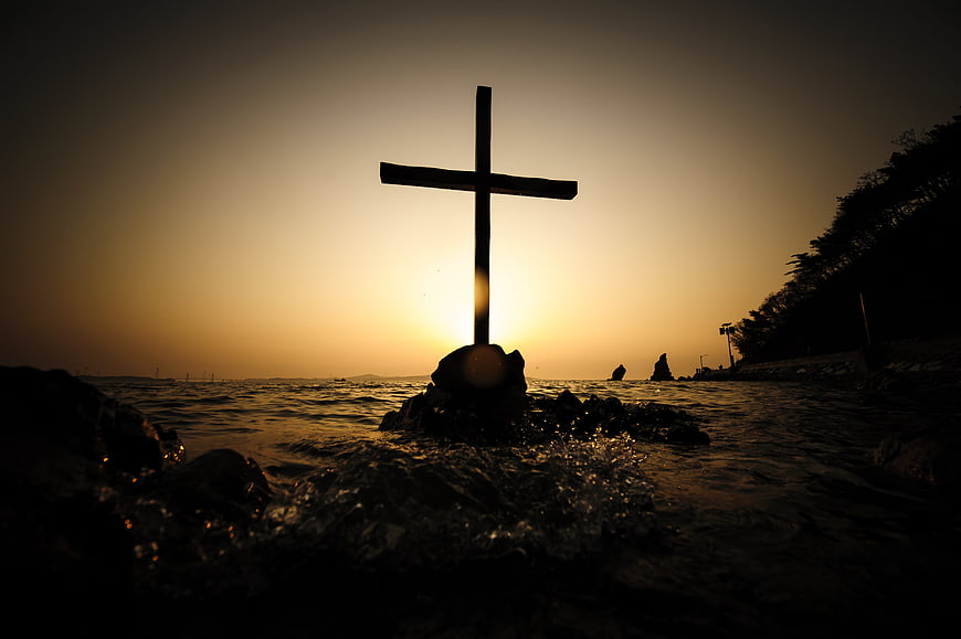 Silhouette of Cross on Rocky Shore at Sunset