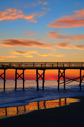 Silhouette of wooden pier at sunset over ocean waves