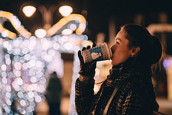 Woman drinking hot coffee at Christmas market night