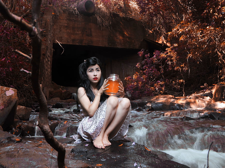 Woman holding glowing jar in stream near tunnel