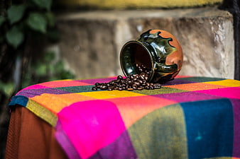Spilled coffee beans from ceramic pot on colorful textile
