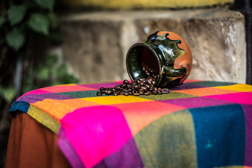 Spilled coffee beans from ceramic pot on colorful textile