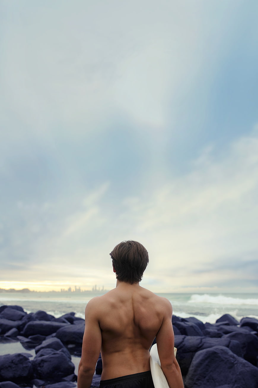 Muscular Surfer Looking at Ocean Horizon from Rocks