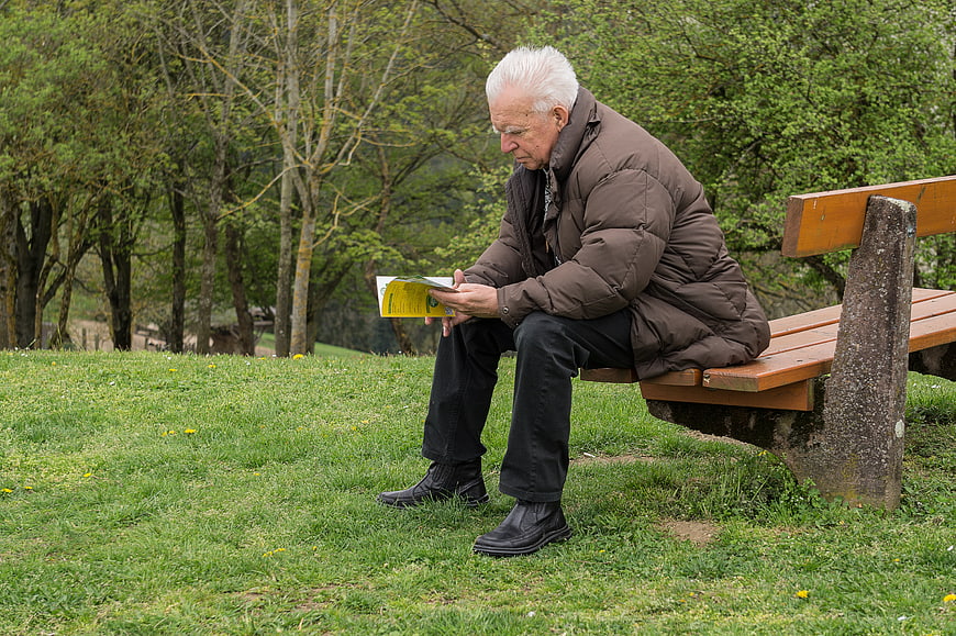 Senior man reading book on park bench in spring