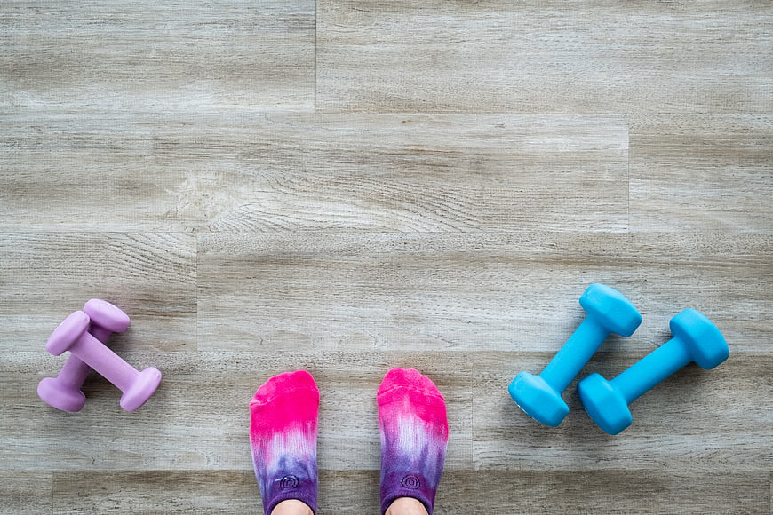 Top view of feet in colorful socks with dumbbells on wooden floor