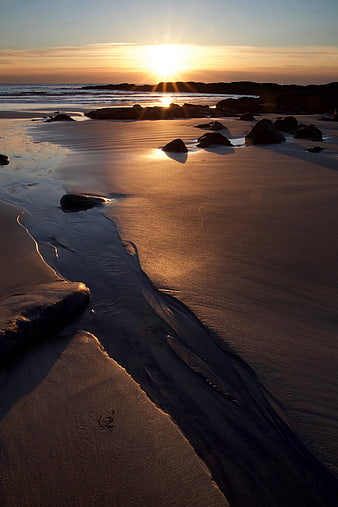 Golden Sunrise Over Sandy Beach with Rocks and Ocean Waves