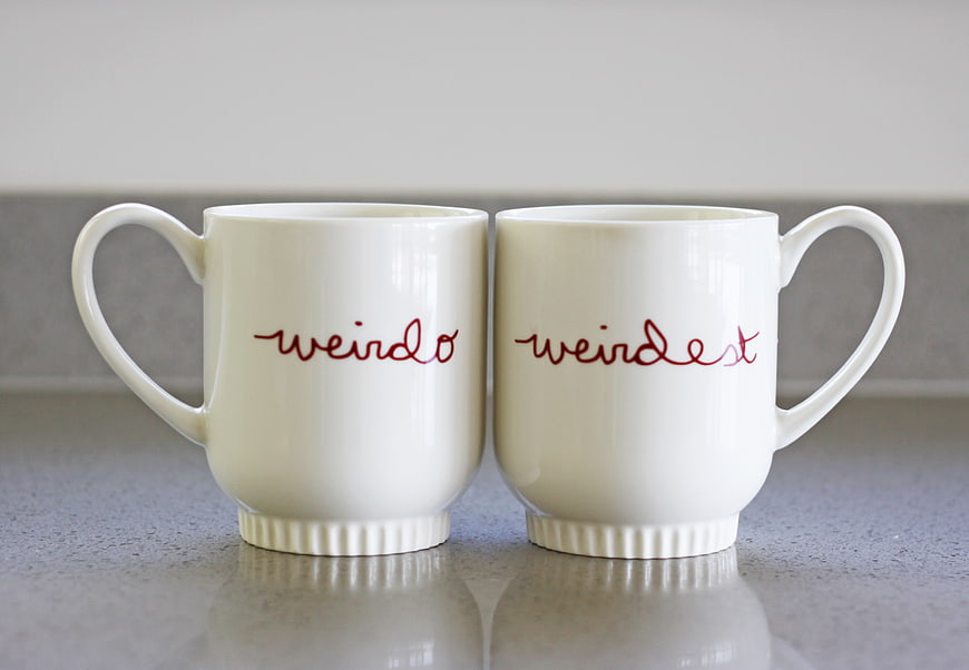 Two white mugs with red cursive text on gray countertop