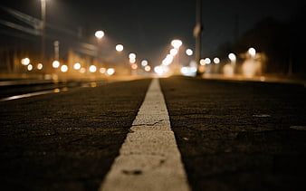 Low angle night shot of road with white line and bokeh lights