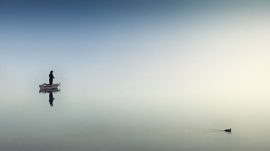 Solitary fisherman in boat on misty calm lake