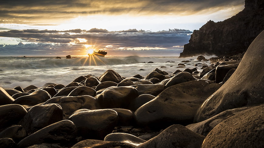 Dramatic sunset over rocky beach with smooth boulders and ocean waves