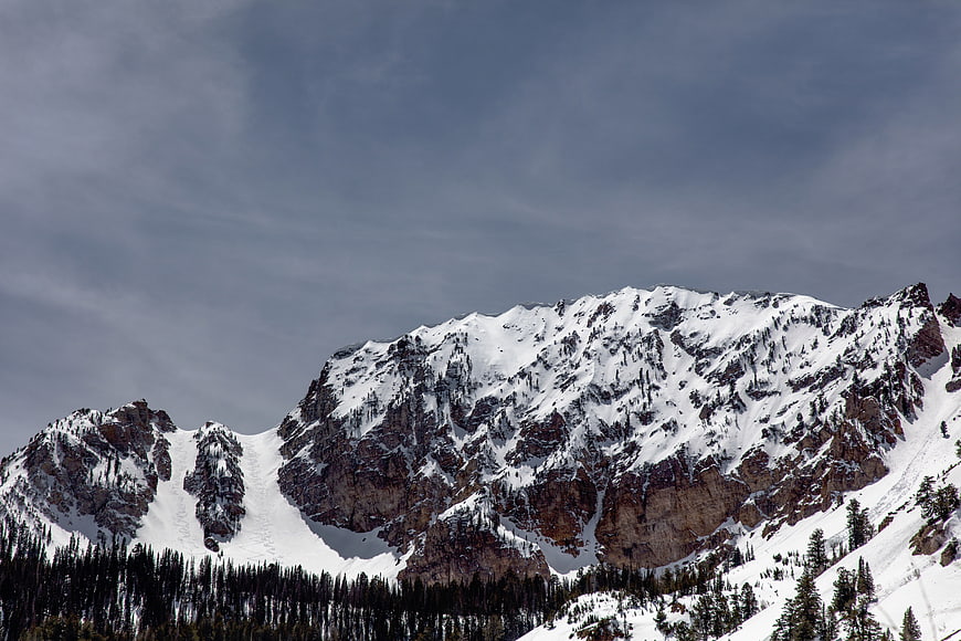 Snow-covered mountain peaks with pine forest and cloudy sky