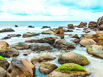 Rocks with green moss on a tropical beach with ocean waves