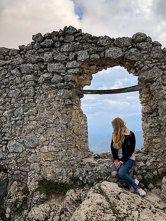 Woman sitting in stone ruins looking at mountain landscape