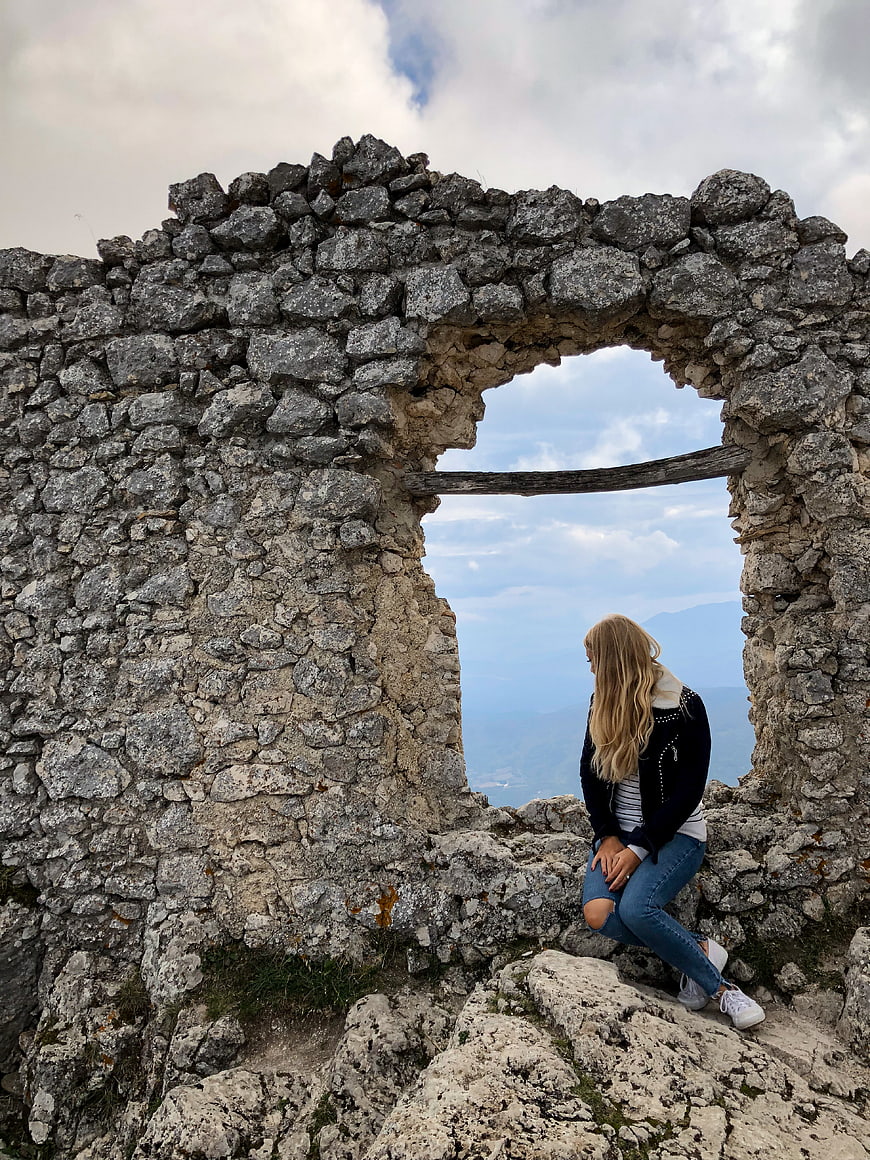 Woman sitting in stone ruins looking at mountain landscape