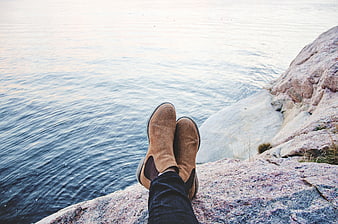 Relaxed feet in boots on rocky shore overlooking calm water