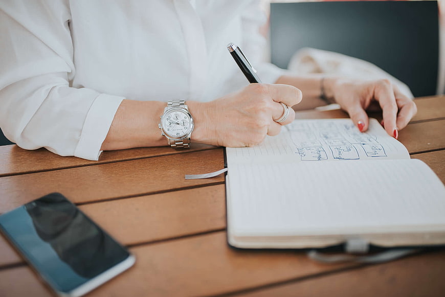 Woman Writing in Notebook at Wooden Table