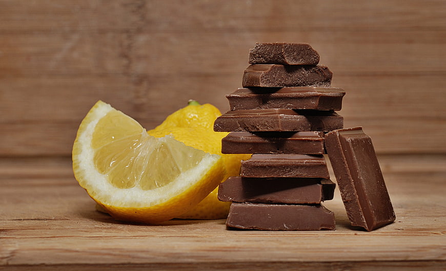 Dark Chocolate Bar Pieces Stacked Next To Fresh Lemon Slices