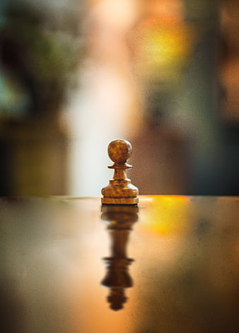 Wooden chess pawn on reflective surface with warm bokeh background