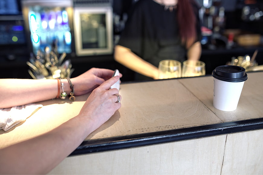 Woman using smartphone at cafe counter with coffee