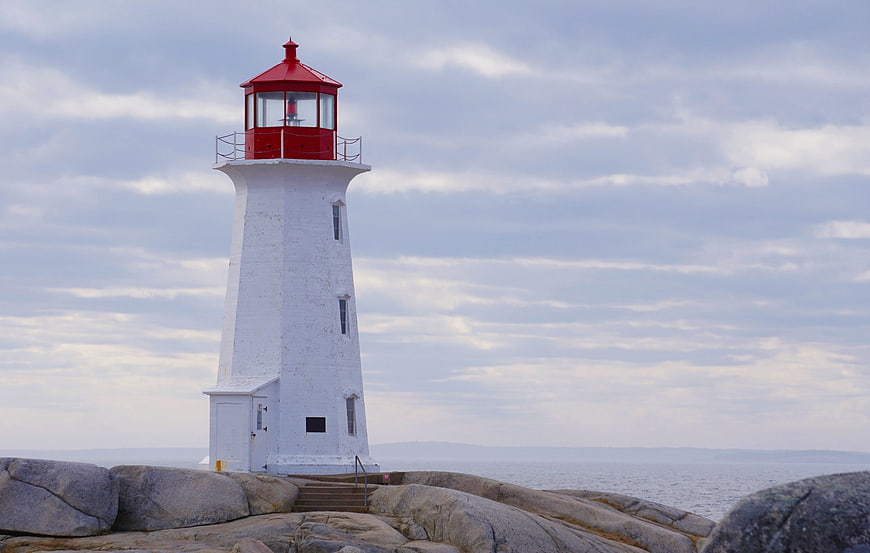 White Lighthouse With Red Roof On Rocky Coastline